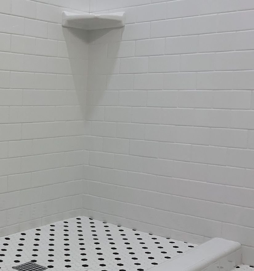 White tile shower with a corner shelf and mosaic shower base