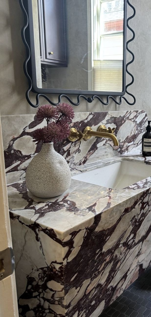 Veined marble vanity with a waterfall edge and brass fittings