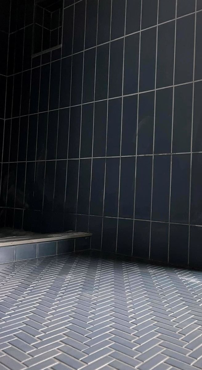 Dark vertical shower wall tile meeting a herringbone tile floor