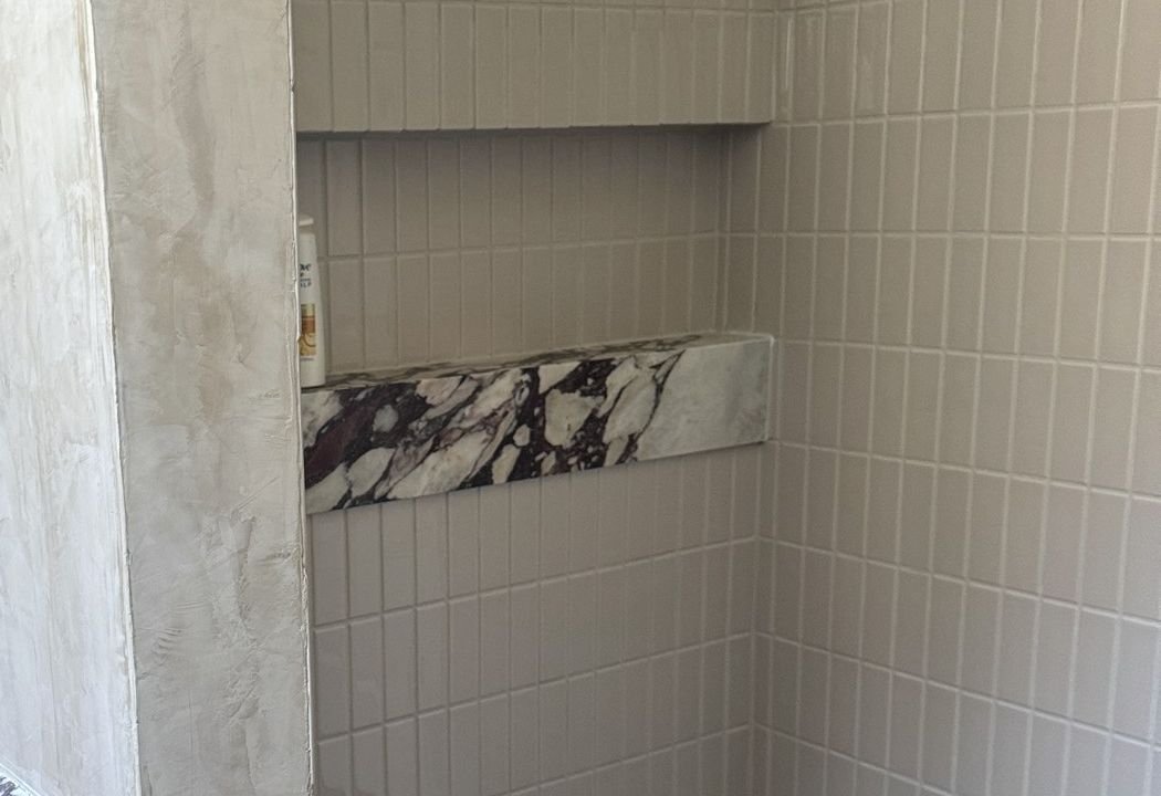 Shower niche with a veined stone shelf set into pale wall tile